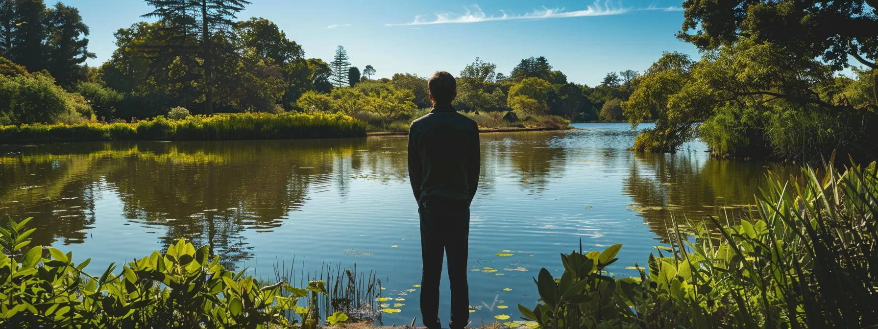 a serene individual standing in front of a tranquil lake, surrounded by lush green trees and clear blue skies, reflecting on their journey into psych-k.