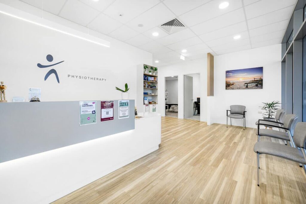 A clean and modern physiotherapy clinic reception area with chairs, health posters, and a beach scene painting.