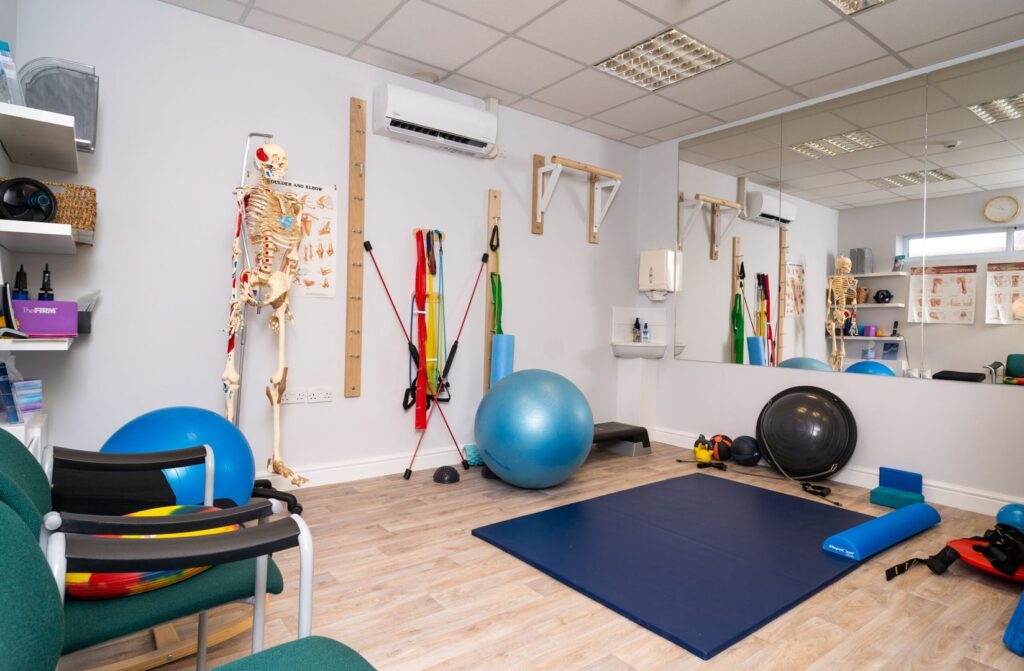 Physiotherapy clinic interior with exercise equipment like balls, mats, and resistance bands, and an anatomical skeleton model.