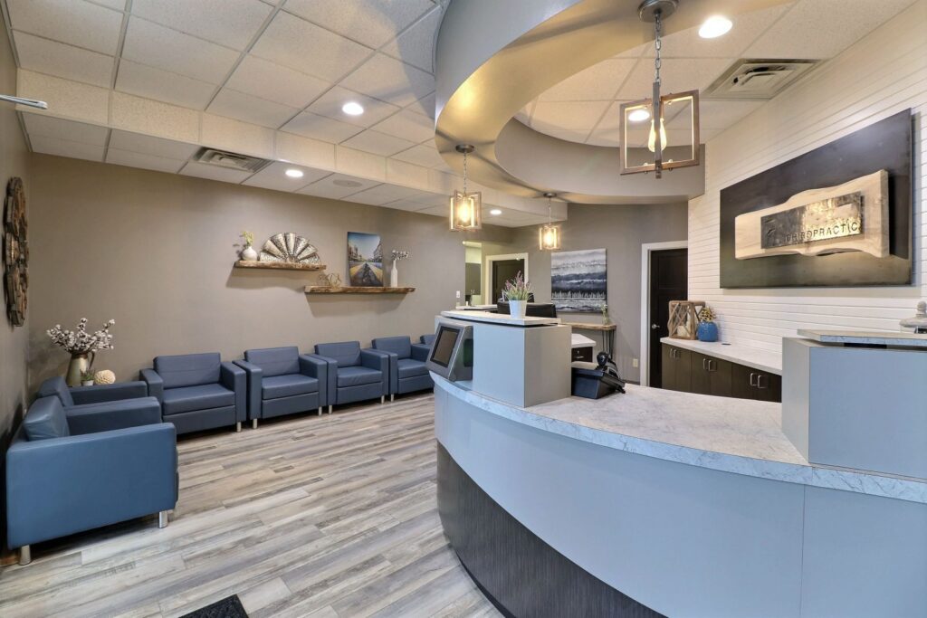 Interior view of a chiropractic clinic's reception desk and waiting area with blue chairs and elegant decor