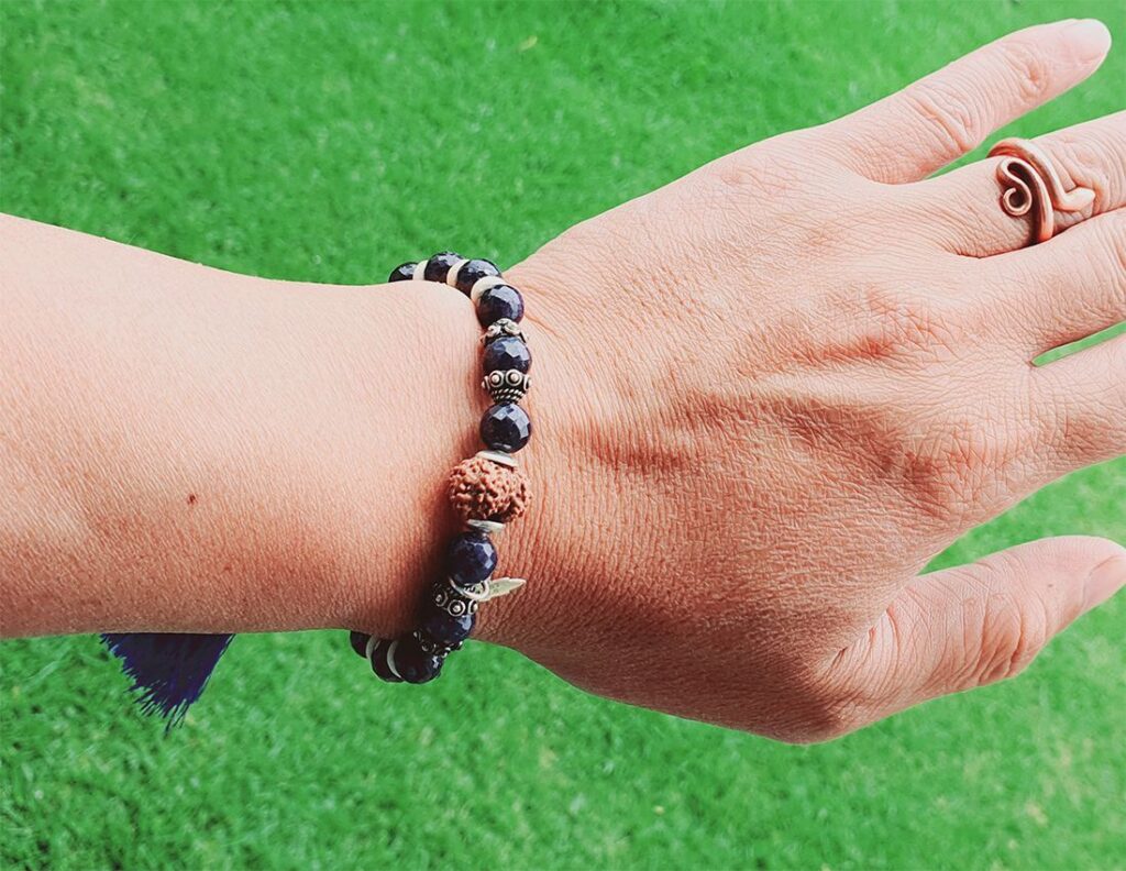 Close-up of a hand wearing a 14 Mukhi Rudraksha and Blue Sapphire Bracelet with Third-eye Chakra Pendant