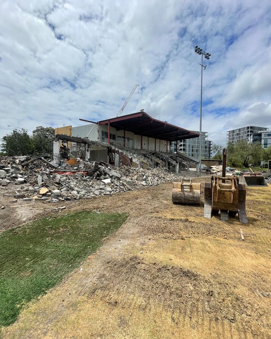 Partially demolished grandstand with heavy machinery and debris in an urban area.