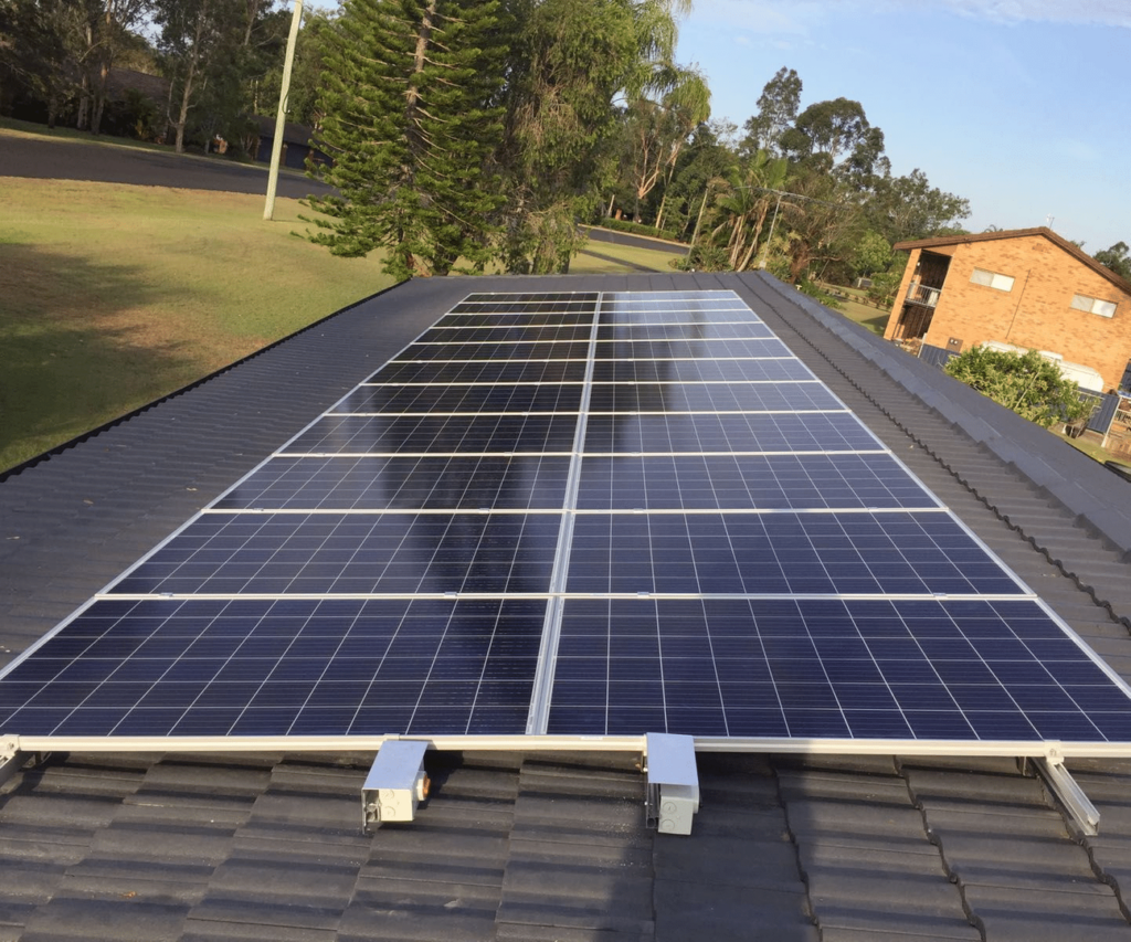 Solar panels installed on a residential rooftop with trees and another house in the background.