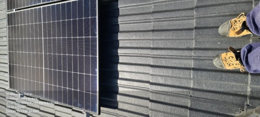 Solar panels installed on a corrugated metal roof with an installer's feet visible.