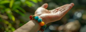 a hand holding a colorful gemstone bracelet against a backdrop of nature.