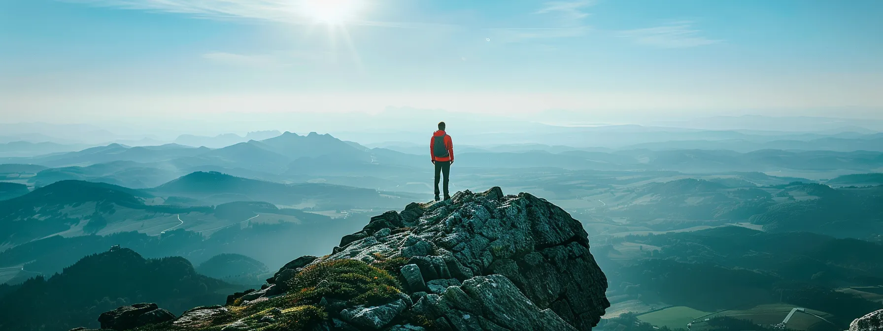 a person standing triumphantly at the top of a mountain, gazing out at a vast landscape with a determined expression.