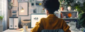 a person sitting at a desk with a laptop open, looking through various online mindset coaching services on the screen.