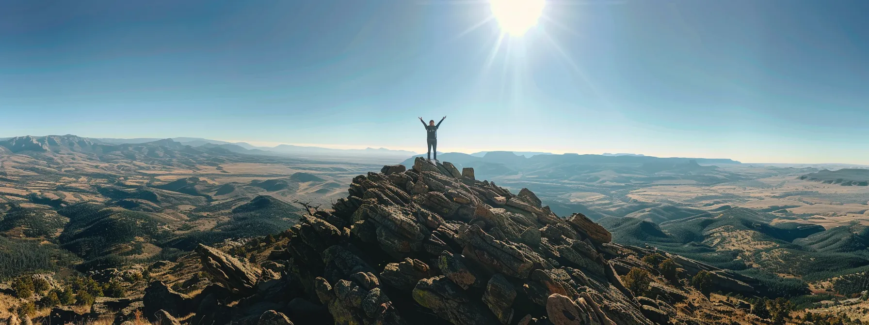 a person standing at the top of a mountain, arms raised triumphantly, overlooking a vast landscape, symbolizing overcoming limiting beliefs and unlocking their full potential.