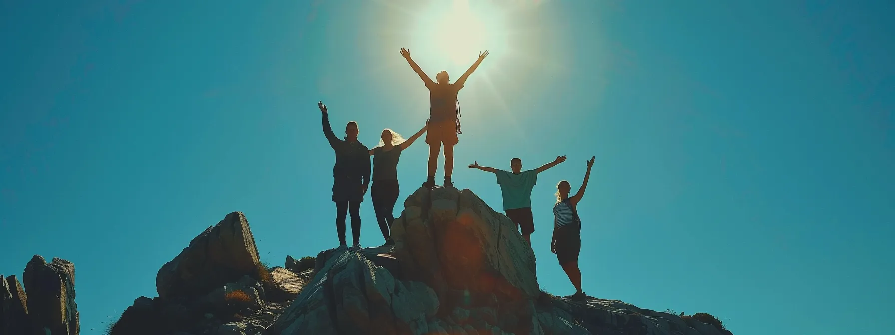 a person standing on top of a mountain, arms raised victoriously, with a clear blue sky and supportive friends cheering in the background.