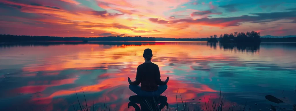 a peaceful, serene sunset over a tranquil lake reflecting the colorful sky, with a person meditating on the shore, surrounded by a sense of calm and healing vibes.