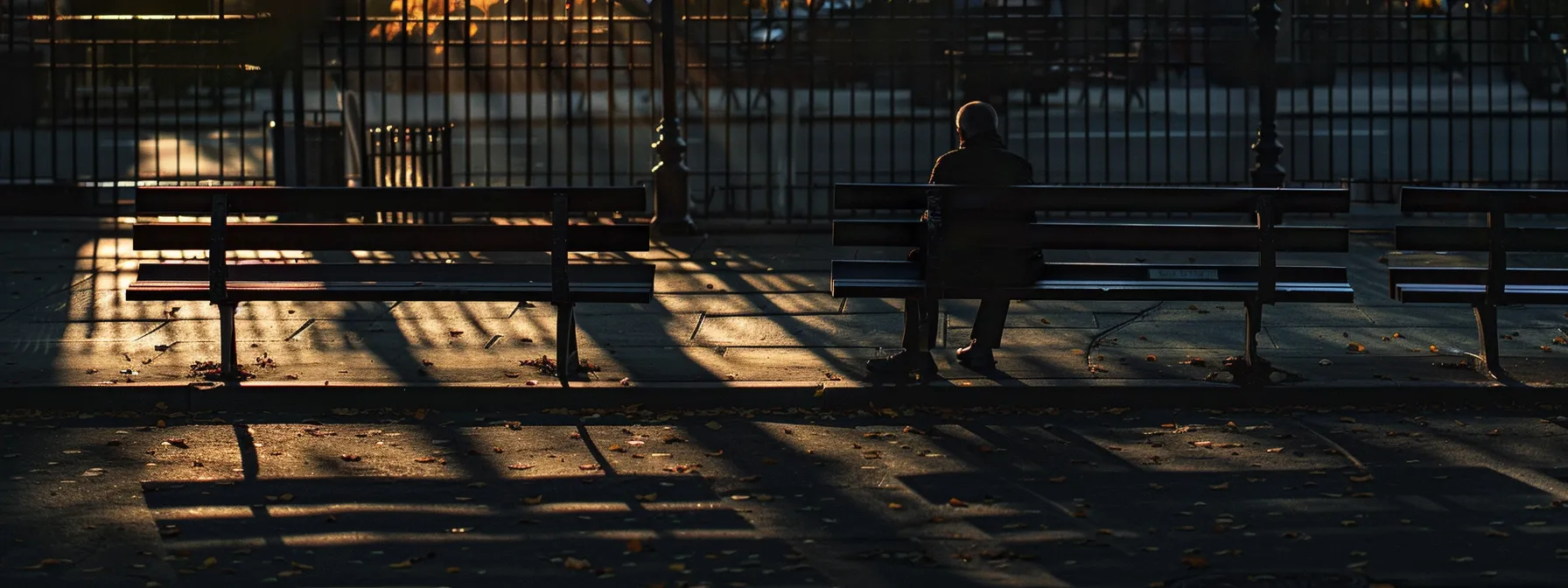 a person sitting on a park bench, visibly tense and anxious, with a shadow of a traumatic event replaying in their mind.