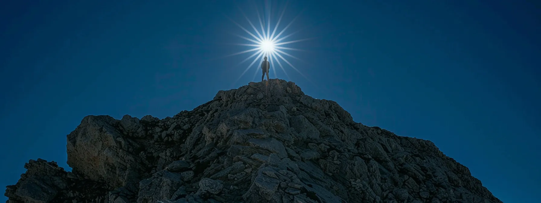 a person standing confidently atop a mountain, with a bright sun shining overhead, exuding unwavering faith in their abilities.