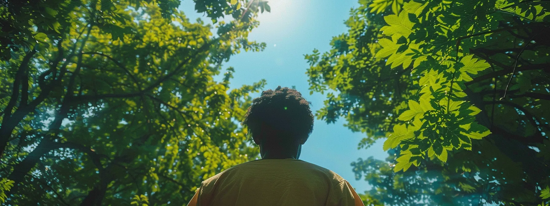 a person standing in a peaceful forest, surrounded by vibrant green trees and a clear blue sky, symbolizing the connection with the subconscious mind for healing and growth through psych-k techniques.