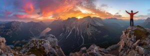 a person standing on a mountaintop, arms outstretched, looking out at a breathtaking sunset.